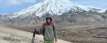 Cameron Fetter in hiking gear standing in front of a snow capped mountain in Alaska (Katmai National Park)