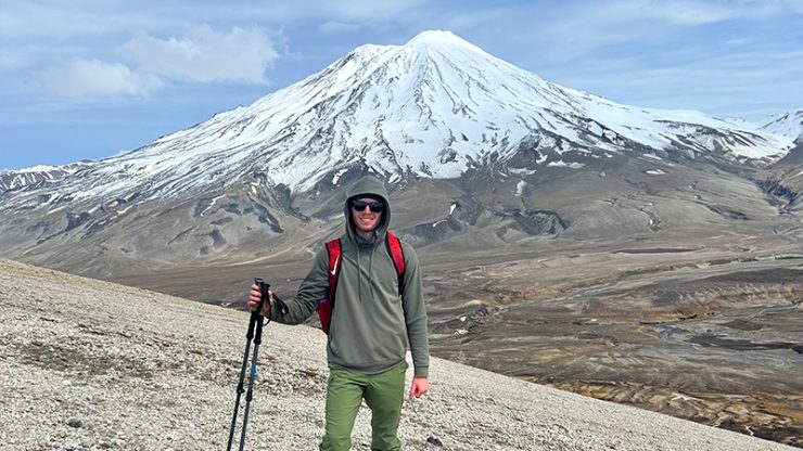Cameron Fetter in hiking gear standing in front of a snow capped mountain in Alaska (Katmai National Park)
